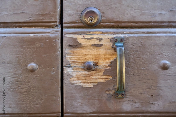 Fototapeta Close-up of an old, weathered wooden door, showing chipped paint, a metal handle, and a deadbolt lock