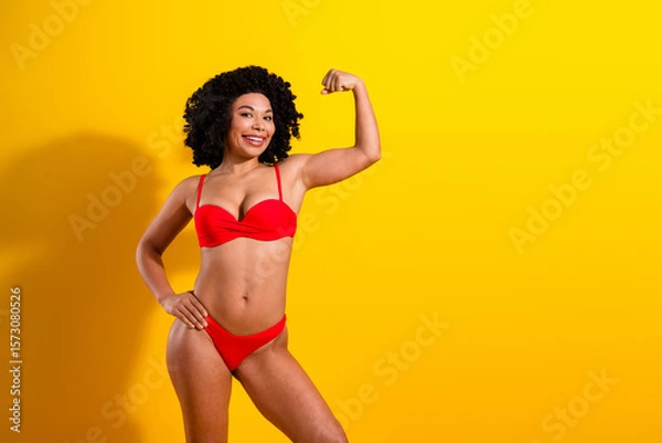 Fototapeta Confident woman in red swimsuit posing against a vibrant yellow background, emphasizing strength, beauty, and self-assurance.