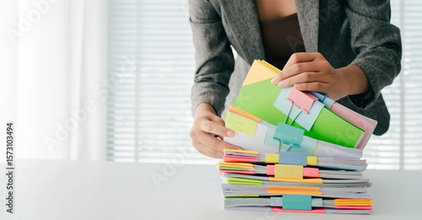 Fototapeta Young female employee is working with a pile of documents to search for information and check documents on the table. Document search concept.