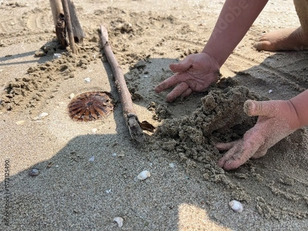 Fototapeta Child playing with wet sand next to jellyfish