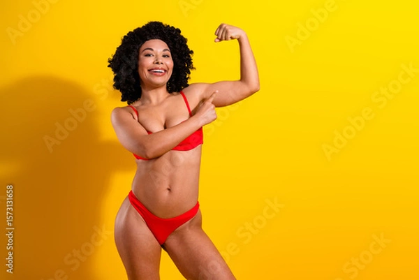 Fototapeta Charming young woman in red lingerie smiling and posing against a vibrant yellow background emphasizing self-esteem