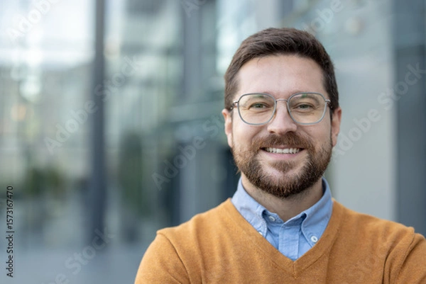 Fototapeta Close-up portrait of a young smiling and successful man standing outside and smiling at the camera
