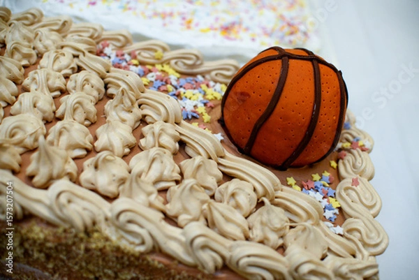 Fototapeta Chocolate cake that is decorated with chocolate cream, colorful stars and a figure made in the shape of a basketball