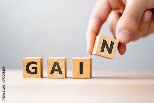Fototapeta A hand rearranging wooden blocks to form the word GAIN, symbolizing growth, success, and achievement in personal or professional development.