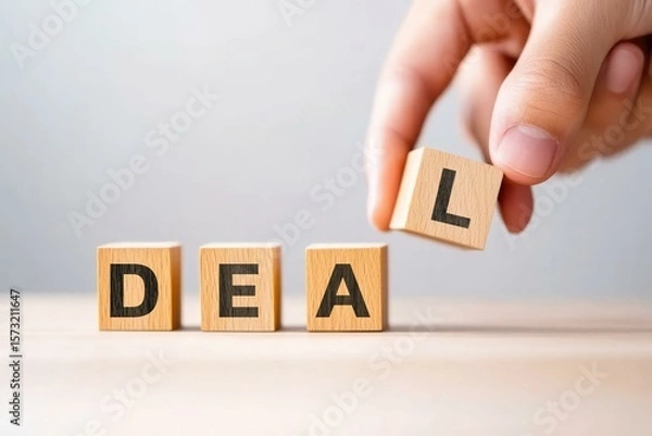 Fototapeta A hand rearranges wooden blocks to spell out the word 'DEAL', representing a business agreement or transaction concept in a professional setting.