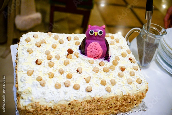 Fototapeta A birthday cake decorated with small and large hazelnuts and a figure in the shape of a purple owl is on the table waiting to be served