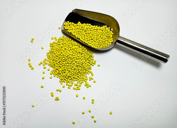 Fototapeta Yellow plastic masterbatch, polymer carries colorful pigments with small scoops poured into a white background, suitable for product catalog design of industrial plastic manufacturing company profiles