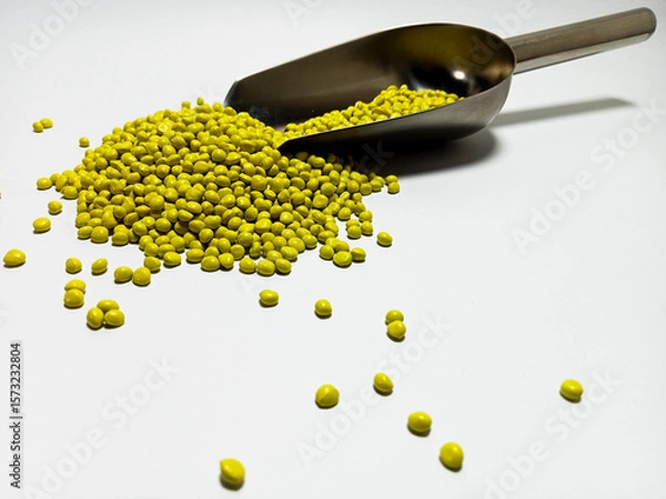 Fototapeta Yellow plastic masterbatch, polymer carries colorful pigments with small scoops poured into a white background, suitable for product catalog design of industrial plastic manufacturing company profiles