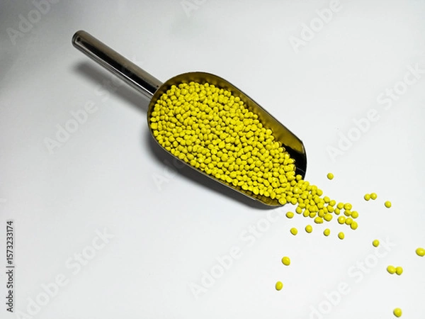 Fototapeta Yellow plastic masterbatch, polymer carries colorful pigments with small scoops poured into a white background, suitable for product catalog design of industrial plastic manufacturing company profiles