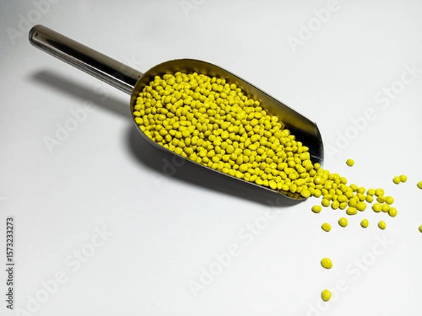 Fototapeta Yellow plastic masterbatch, polymer carries colorful pigments with small scoops poured into a white background, suitable for product catalog design of industrial plastic manufacturing company profiles