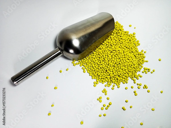 Fototapeta Yellow plastic masterbatch, polymer carries colorful pigments with small scoops poured into a white background, suitable for product catalog design of industrial plastic manufacturing company profiles
