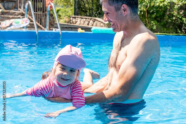 Fototapeta Family Dad and Daughter Swim in Pool on Sunny Day in Summer with Inflatable Ring