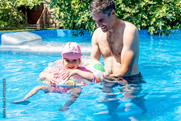 Fototapeta Family Dad and Daughter Swim in Pool on Sunny Day in Summer with Inflatable Ring
