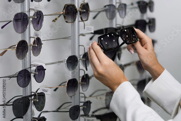 Fototapeta Close-up of hands of a young woman who chooses sunglasses on the showcase for purchase in an optical store. Optometry, eyesight, eyeglasses, accessories, fashion, lifestyle
