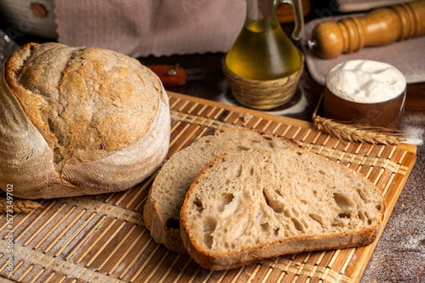 Fototapeta Healthy, organic, whole and sliced ​​homemade sourdough bread with ham and cheese on a wooden table and kitchen utensils with an airy crumb and crispy crust. 