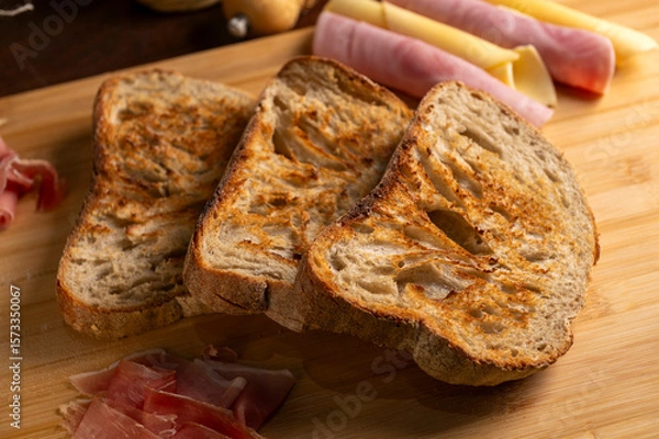 Fototapeta Healthy, organic, whole and sliced ​​homemade sourdough bread with ham and cheese on a wooden table and kitchen utensils with an airy crumb and crispy crust. 