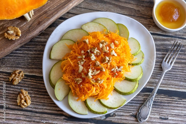 Fototapeta Bright healthy organic autumn harvest salad made of pears, pumpkin, walnut and honey with fork on wooden table. Top view