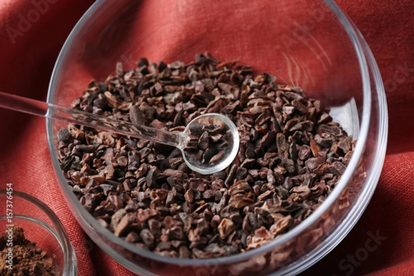 Fototapeta Bowl with cocoa nibs on color cloth background