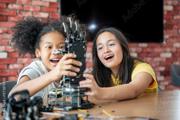 Fototapeta Children Learning Robotics, Young Girls Engaged in Robotics and STEM Learning, Diverse Kids Building a Robot Arm in a Science Workshop, Two Girls Exploring Technology and Innovation