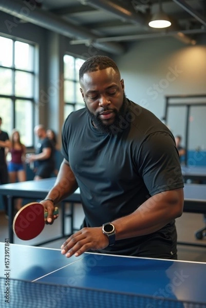 Fototapeta A plus-size black man is playing table tennis in a modern gym with large windows and exercise equipment. The atmosphere is energetic and competitive