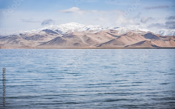 Fototapeta Panorama landscape of Lake Karakul in the Pamir mountains in the Tien Shan against the background of high snowy rocky peaks with clouds, morning panorama of the lake for the background
