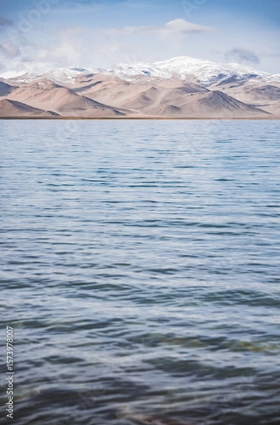 Fototapeta Panorama landscape of Lake Karakul in the Pamir mountains in the Tien Shan against the background of high snowy rocky peaks with clouds, morning panorama of the lake for the background