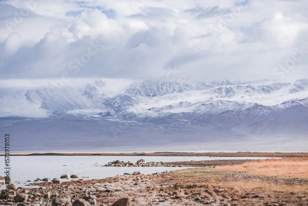 Fototapeta Rocky shore of Lake Karakul and blue water of a high mountain lake against the background of rocky mountain slopes in the Pamirs in the Tien Shan, panoramic landscape for background