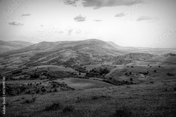 Fototapeta Rolling hills stretch to the horizon under a cloudy sky, capturing the vastness of the landscape with a monochromatic tone.