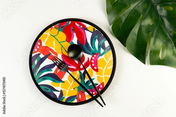 Fototapeta Top view of black tray, colorful plate, black cutlery on white background. Exotic plant plate, monstera palm leaf, summer picnic. Flat lay, copy space.