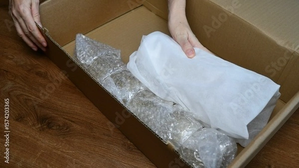 Obraz Packing up fragile tableware into plastic bubble wrapping inside cardboard box