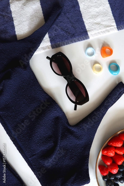 Obraz Navy swimsuit, striped beach towel, sunglasses, colorful rings and plate with berries. Top view.