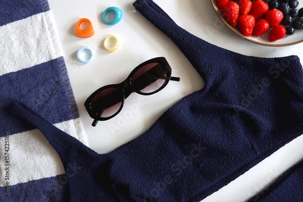Obraz Navy swimsuit, striped beach towel, sunglasses, colorful rings and plate with berries. Top view.