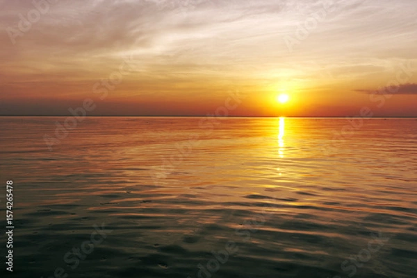 Fototapeta Beautiful sunset over the ocean with soft waves and glowing sky in warm yellow, orange, and red tones. Peaceful seascape evoking calm, romance, and evening serenity.