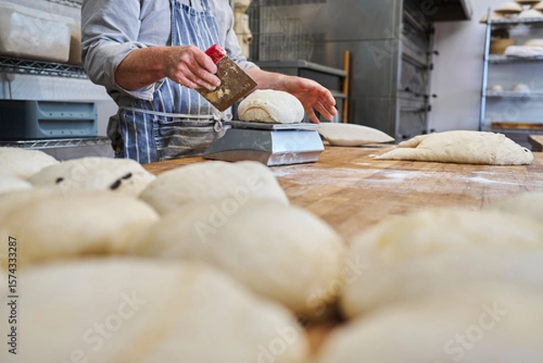Obraz Close up of baker cutting and weighing batch of dough to make individual loaves in bakery