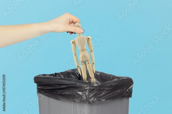 Fototapeta Throw wooden man, in the trash, outstretched hand with wooden mannequin in front of trash can