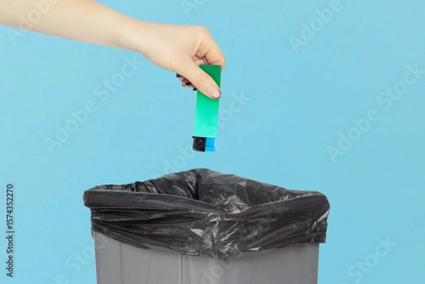 Fototapeta throw the lighter in the trash, outstretched hand with a lighter in front of the trash can, the concept of the dangers of smoking cigarettes, quitting smoking