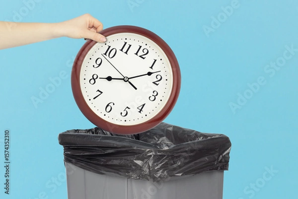 Fototapeta Throw round wall clock in the trash, outstretched hand with round wall clock in front of trash can
