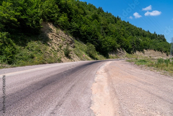 Fototapeta Winding road in the countryside in the mountains with blue sky and clouds.