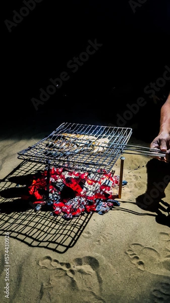 Fototapeta Grilled fish over open fire in nature, rustic outdoor cooking with flames and smoke

