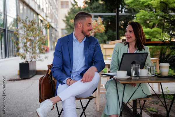 Fototapeta Two business colleagues are sitting at an outdoor cafe, enjoying a coffee break after work, discussing projects, and relaxing together in a friendly atmosphere