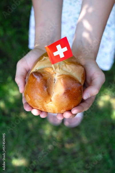 Fototapeta Swiss national August bread bun with a swiss flag in child hands.