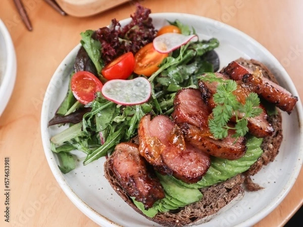 Fototapeta close up of sourdough toast with avocado slice and duck breast in yuzu sauce. Lecttuce and cherry tomato on the side on a white plate 