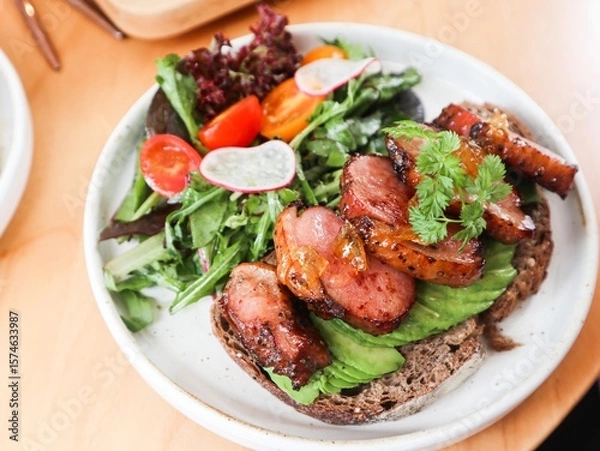 Fototapeta close up of sourdough toast with avocado slice and duck breast in yuzu sauce. Lecttuce and cherry tomato on the side on a white plate 