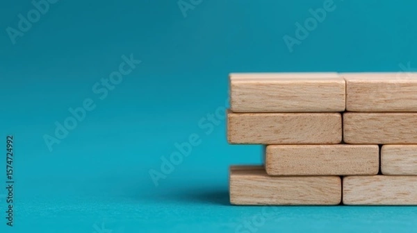 Obraz Stacked wooden blocks arranged in a neat formation on a turquoise surface with a plain background.