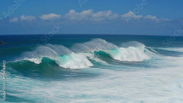 Fototapeta Ocean waves crashing under a clear blue sky with some clouds, creating a dynamic and refreshing scene.