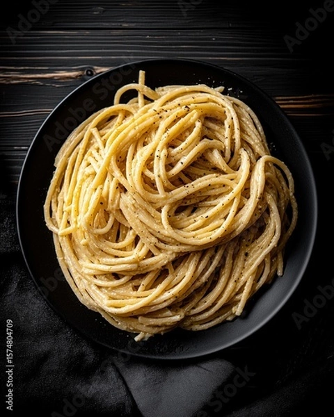 Fototapeta A top-down view of a gourmet pasta dish, arranged in a natural swirl on a dark plate. The scene is set with moody, dramatic lighting, creating a painterly, rustic still life.