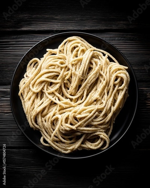 Fototapeta A top-down view of a gourmet pasta dish, arranged in a natural swirl on a dark plate. The scene is set with moody, dramatic lighting, creating a painterly, rustic still life.