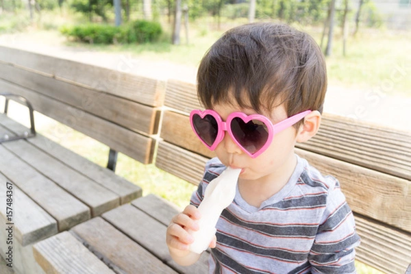 Obraz ハートのサングラスをかけた男の子がスイーツを楽しむ夏の屋外ポートレート｜家族レジャー・お祭りイメージに最適な子ども写真