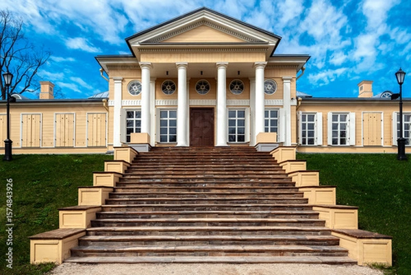 Fototapeta Wooden house with white columns and a wide staircase with stone steps leading to it.
