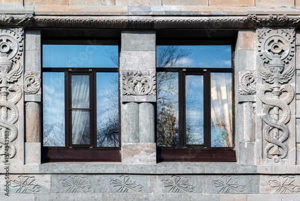 Fototapeta Two rectangular windows with brown frames against a wall of gray blocks with an ornament. From the Windows of the World series.